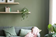 a simple living room with a green accent wall, a grey sofa with green pillows, a couple of shelves and a coffee table, greenery