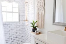 a smal and neutral boho bathoom with white subway tiles and black and white ones, a farmhouse vanity, a macrame hanging and touches of black
