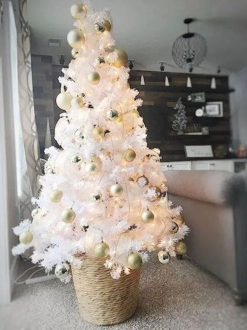 a small Christmas tree in white with gold ornaments and in a basket is a cool and catchy idea for a modern space