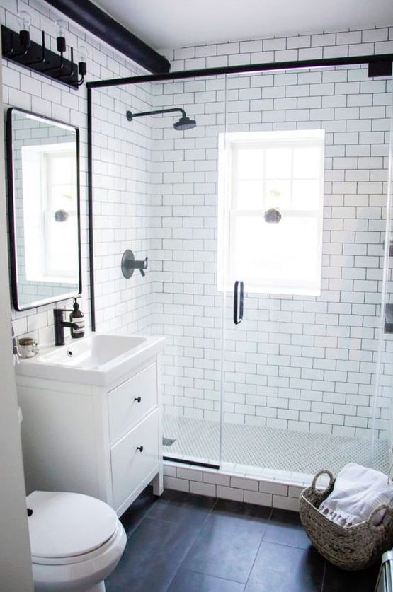 a small and cool bathroom with white subway tiles, black ones on the door, a shower space and touches of black here and there
