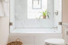 a small modern bathroom with marble tiles, a white tub, marble herringbone tiles, a sink and a basket