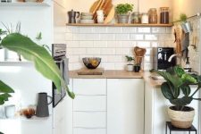 a tiny minimalist kitchen in white, with wooden coutnertops and a shelf plus a white subway tile backsplash and pendant bulbs