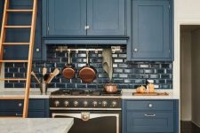 a vintage-inspired navy kitchen with glossy navy subway tiles, white marble countertops and metallic touches