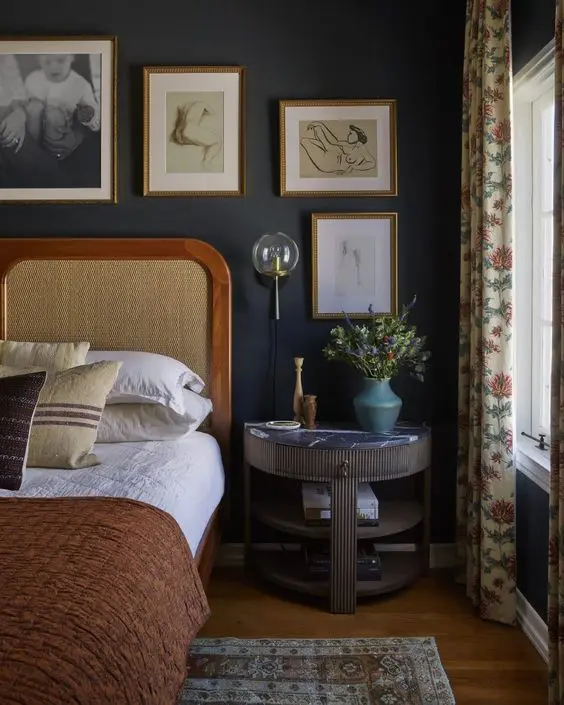 a vintage moody bedroom with soot walls, a bed with a cane headboard, a fluted nightstand, a gallery wall and printed textiles
