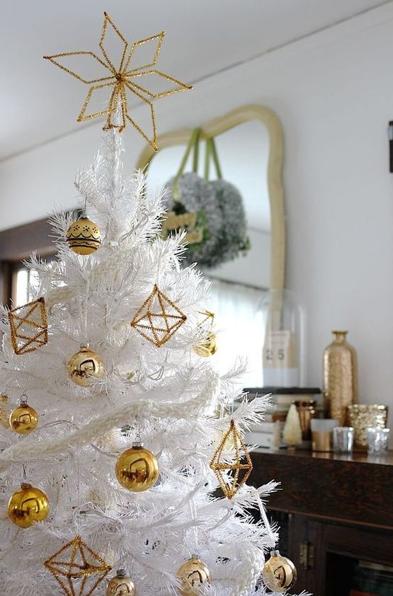a white Christmas tree decorated with gold bauble and himmeli ornaments and a shiny gold star topper