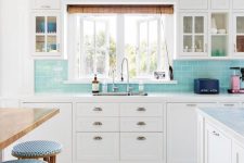 a white coastal kitchen with shaker cabinets, a turquoise subway tile backsplash, a stained table and blue stools