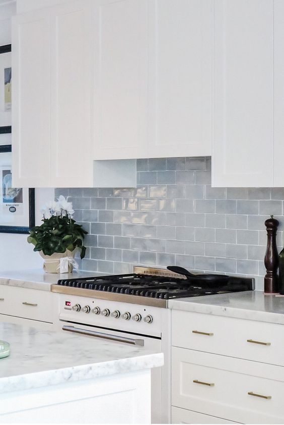 a white farmhouse kitchen with white countertops, a grey subway tile backsplash and gold fixtures