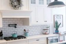 a white farmhouse kitchen with white stone countertops, a white subway tile backsplash, pendant lamps and decor