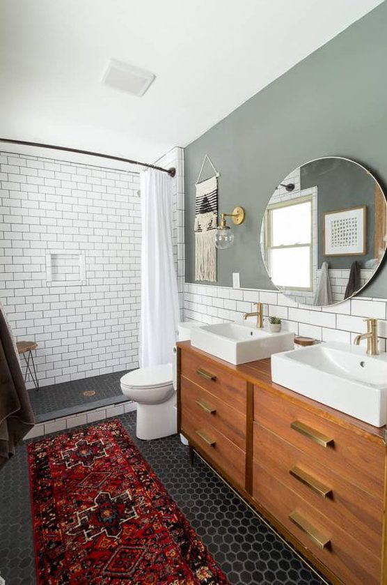 An amazing mid century modern bathroom with white subway tiles and black hex ones, a bright rug and a wooden vanity with gold touches