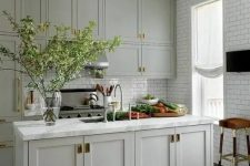 an amazing pale green modern country kitchen with shaker cabients, white subway tiles, brass touches for extra elegance