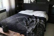 an edgy black and white bedroom with moody black walls, a black bed, a wooden bench, a unique pendant lamp and a gallery wall