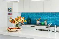 an eye-catchy kitchen with sleek cabinets, a bold blue subway tile backsplash, a large kitchen island and dark stools