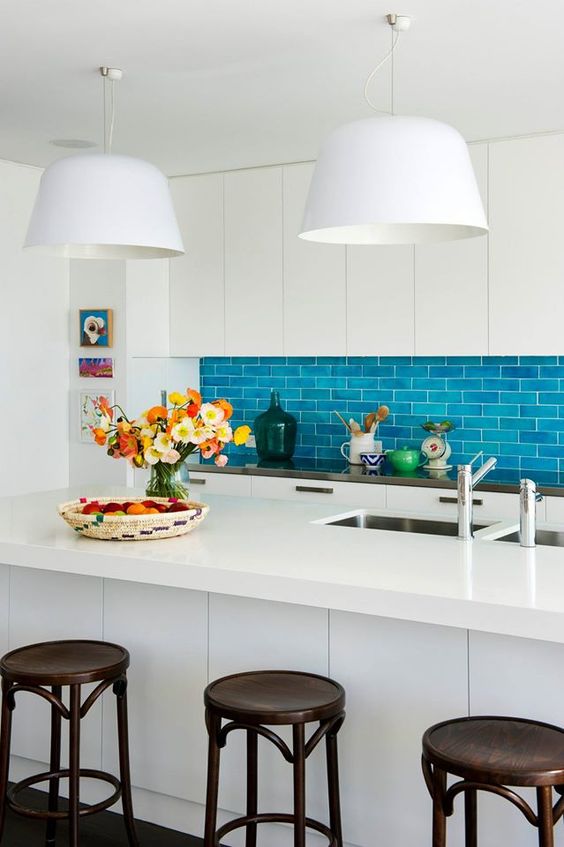 An eye catchy kitchen with sleek cabinets, a bold blue subway tile backsplash, a large kitchen island and dark stools