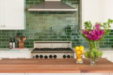 an eye-catchy white farmhouse kitchen with stone and butcherblock countertops, a bold green subway tile backsplash