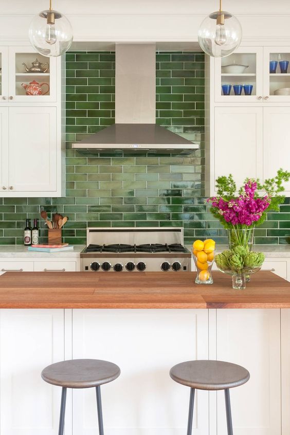 An eye catchy white farmhouse kitchen with stone and butcherblock countertops, a bold green subway tile backsplash
