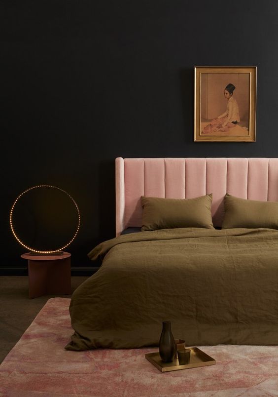 a refined moody bedroom with black walls, a pink upholstered bed and olive green bedding, a nightstand with lights and a blush pink rug is a cool and lovely space