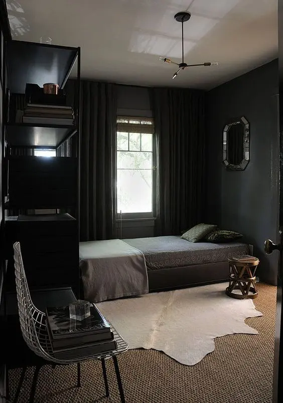 a peaceful black bedroom with a bed next to the window, a large black shelving unit, a bed with printed bedding, a nightstand, a metal chair and layered rugs