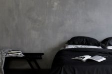 a moody bedroom with plaster walls, a bed with black and white bedding, a black bench and books is a chic and cool idea