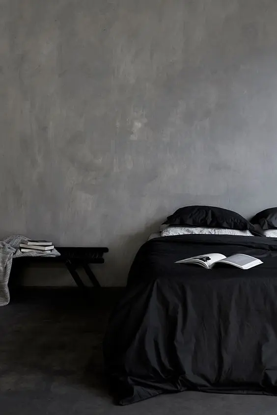 a moody bedroom with plaster walls, a bed with black and white bedding, a black bench and books is a chic and cool idea