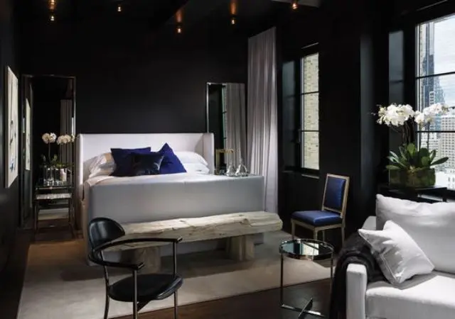 an elegant dark bedroom with a crispy white bed and a raw wood bench for a contrast, lights and mismatching chairs