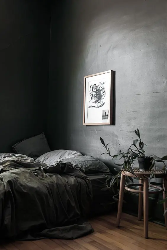 an elegant grey moody bedroom with a tiered glass nightstand, potted plants, grey bedding and peaceful light