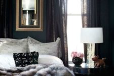 a sophisticated moody bedroom with black walls and curtains, a fur blanket and a framed mirror plus some decor