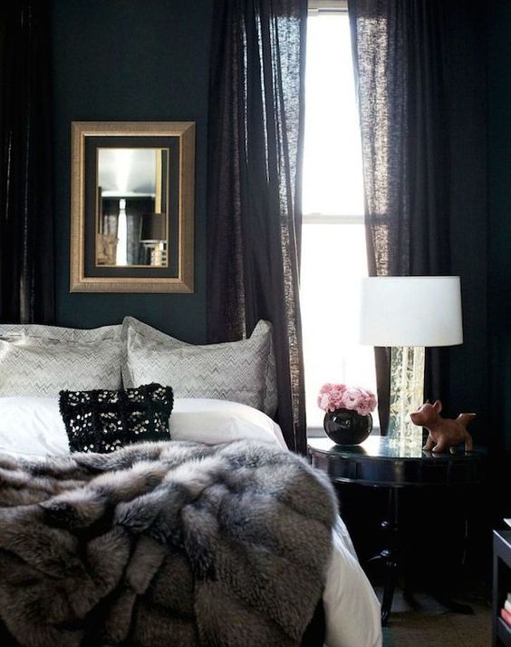 a sophisticated moody bedroom with black walls and curtains, a fur blanket and a framed mirror plus some decor