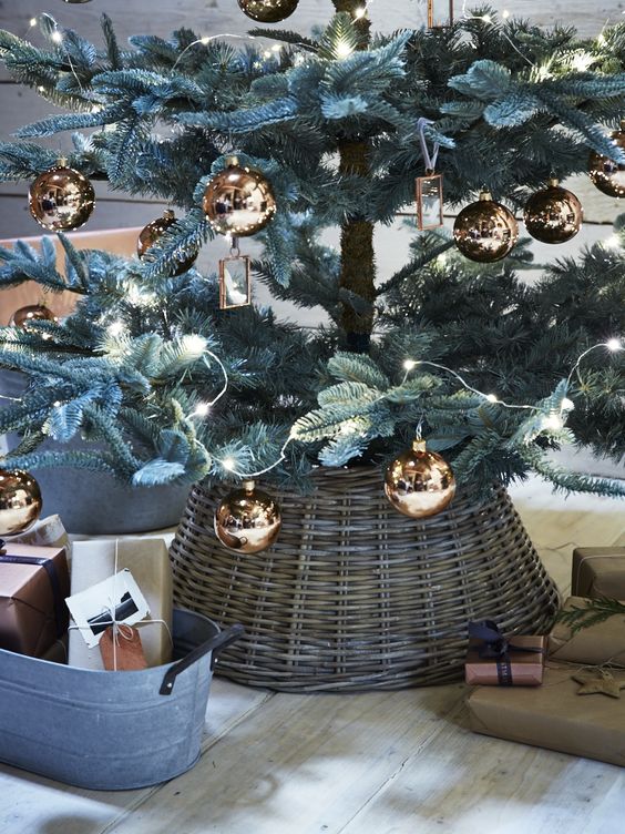 a Christmas tree with copper ornaments and a basket that hides the tree base creates a cozy and lovely feeling in the room due to the rustic touch that the basket brings