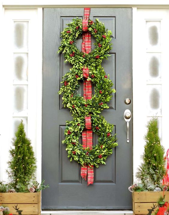 a boxwood wreath tirio on the door, small evergreen trees with lights
