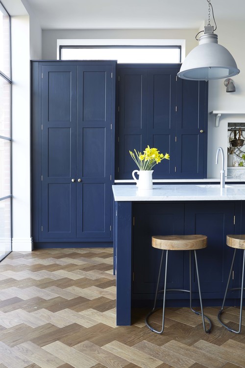 Ligt-colored parquet contrasts with navy cabinets and the kitchen is flooded with light through the window wall