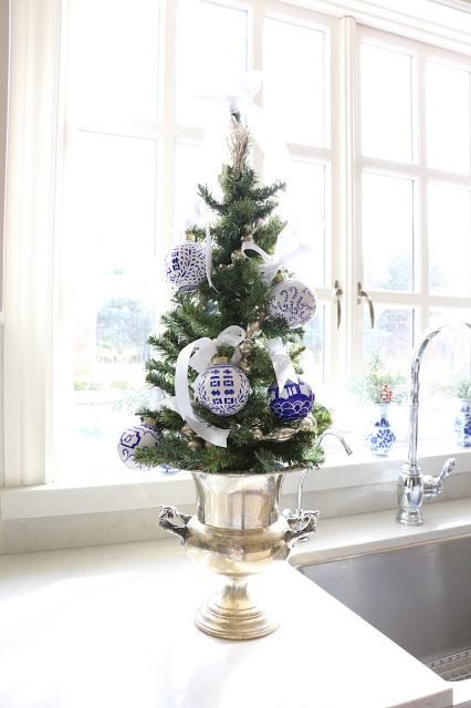 a tabletop tree placed in a gold urn with blue and white ornaments