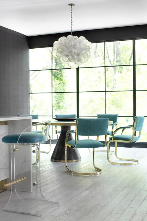 The dining area is located by the window, and the upholstered gilded chairs echo with the lucite ones