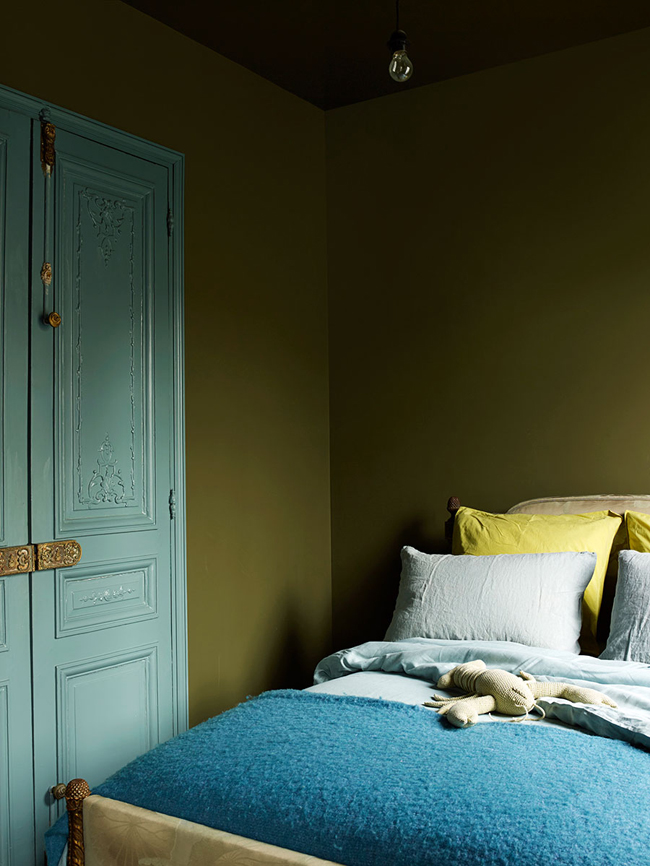 The guest bedroom is decorated in the same moody shade of green as the living room, and there are blue touches added