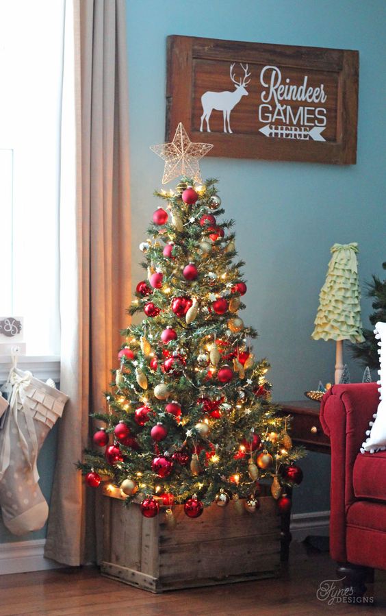 a bright Christmas tree with red and gold ornaments and placed in a rustic crate looks sweet and excessive as this crate creates a harmonious look with the bold tree