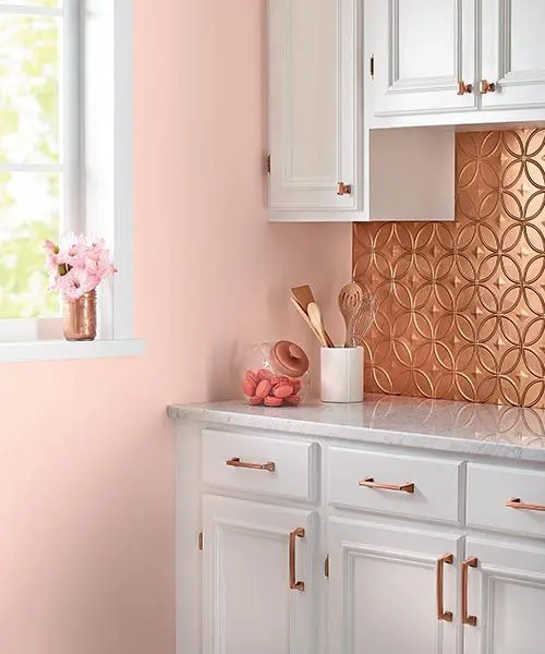 A tin tile backsplash, matching copper cabinet pulls, and serene pink walls make for a charming kitchen corner