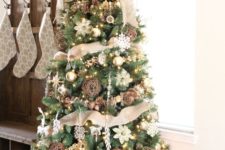 a rustic tree decorated with burlap, gold and white ornaments, snowflakes and lights, pinecones and ribbons in a galvanized bucket