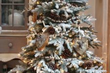 a beautifu rustic flocked Christmas tree with faux taxidermy and large pinecones in a galvanized bucket looks a bit woodland-style