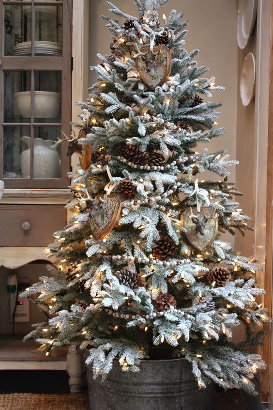 A beautifu rustic flocked Christmas tree with faux taxidermy and large pinecones in a galvanized bucket looks a bit woodland style