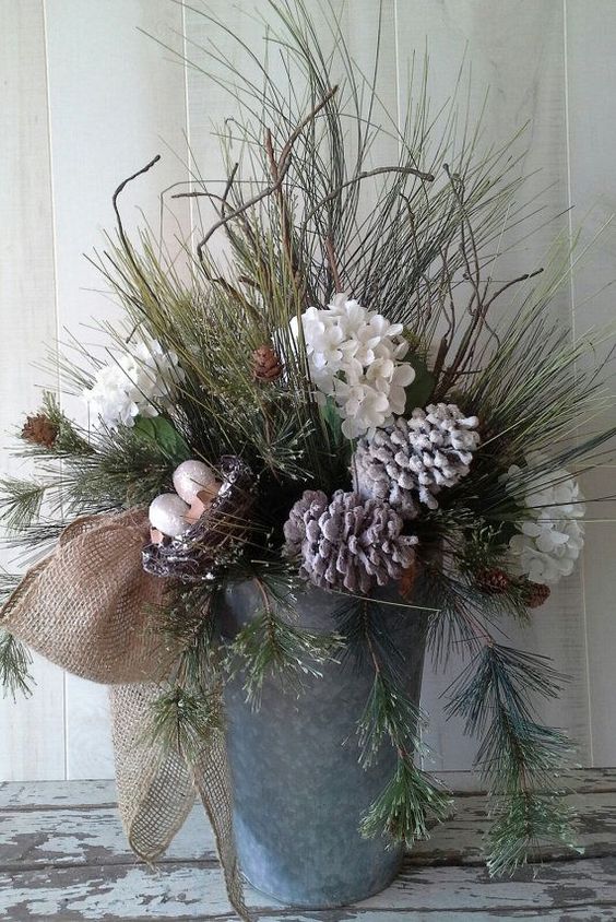 a bucket with evergreens, snowy pinecones and flowers