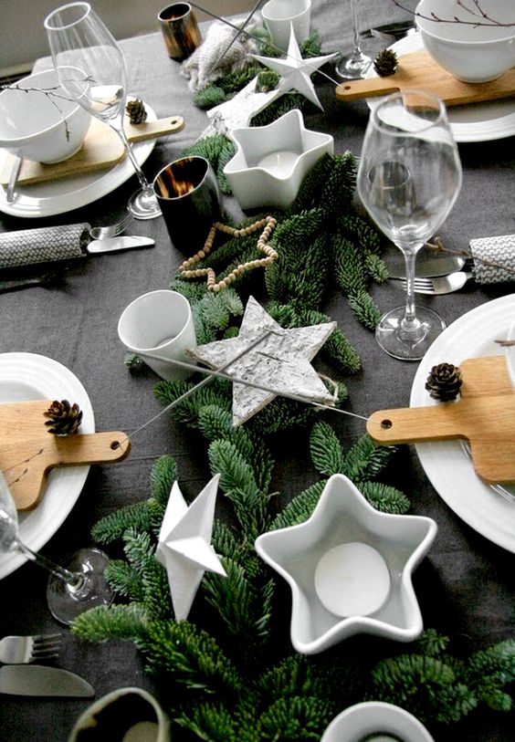 A table setting with faux evergreens, star shaped candle holders and pinecones