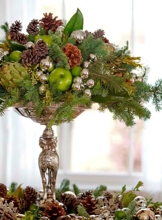 a silver stand with oraments, pinecones, evergreens and ggreen apples