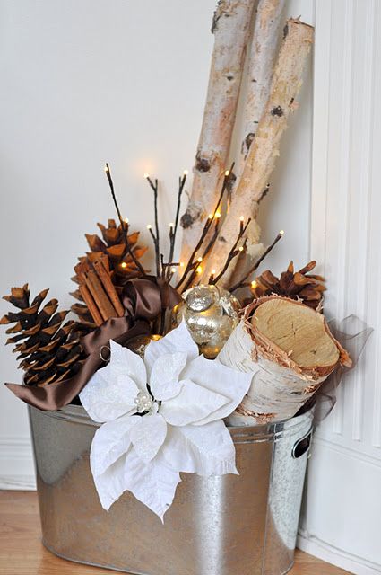 a galvanized bucket with logs, pinecones, lights and fabric