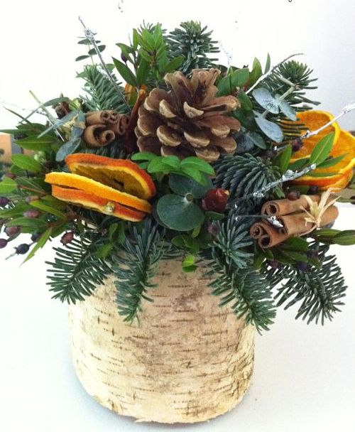 a vase wrapped with bark, evergreens, pincones, citrus and cinnamon sticks