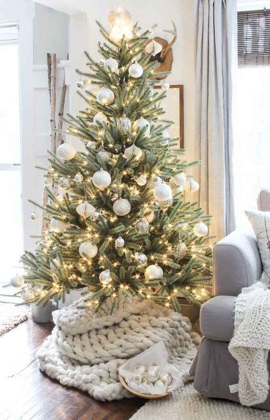 a beautiful Christmas tree with silver and white ornaments, lights and a chunky knit cover is a very cozy and modern piece