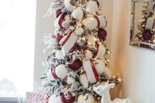 a bold Christmas tree with lights, striped ribbons, red and white ornaments, faux fur and pillows under the tree and some toys