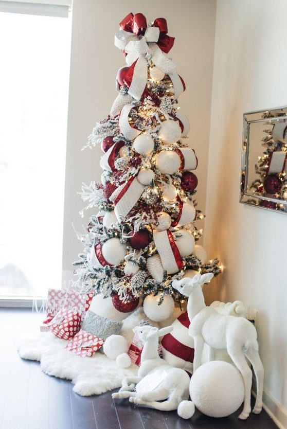 a bold Christmas tree with lights, striped ribbons, red and white ornaments, faux fur and pillows under the tree and some toys