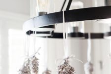 a bulb chandelier decorated with snowy pinecones is a cool and chic idea for the holidays, it’s quite rustic