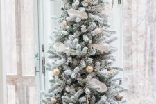 a catchy flocked Christmas tree with white ribbon and gold ornaments plus a basket base cover is a stylish idea