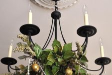 a classic candle-style chandelier decorated with greenery, beads and gold glitter ornaments for the holidays