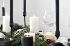 a contrasting Christmas table with an evergreen runner with snowy pinecones, black and white faceted ornaments, black and white candles and white plates plus black napkins